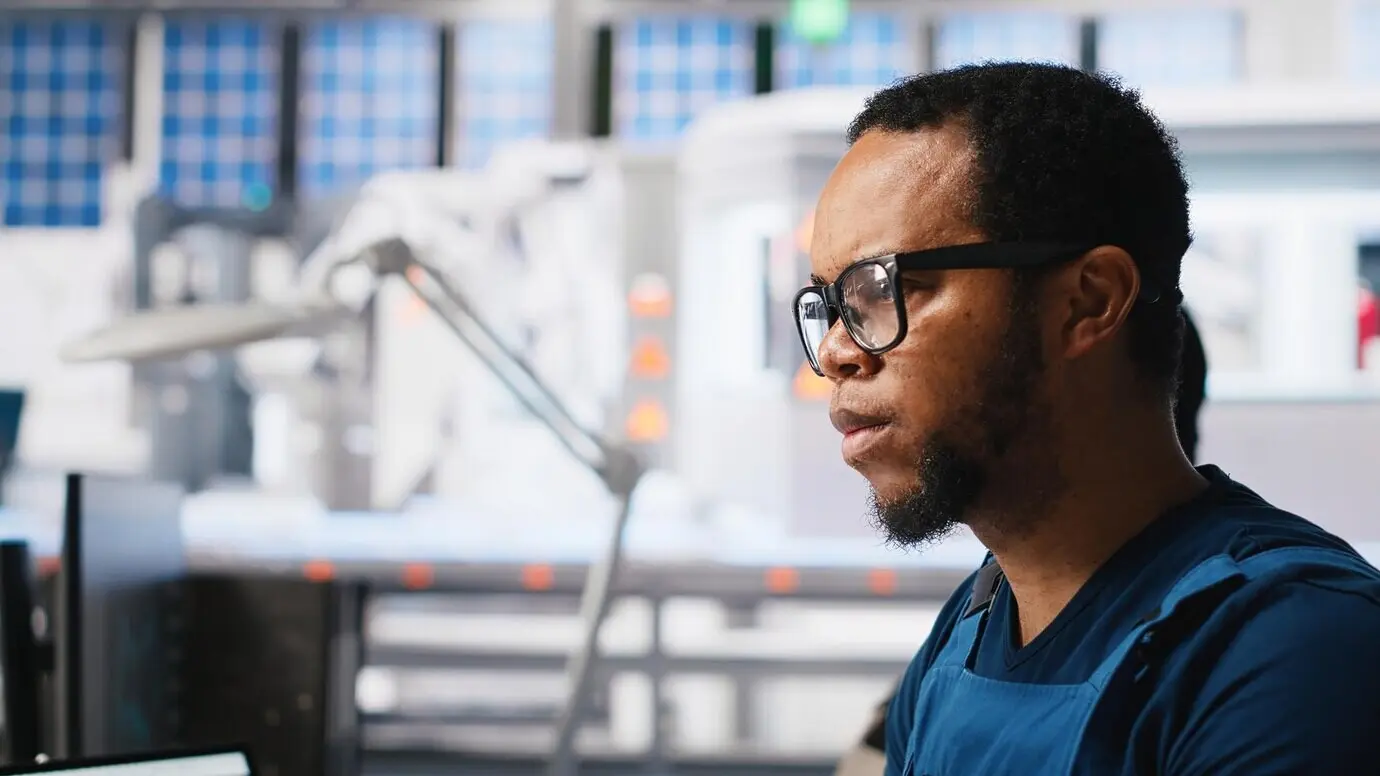 An African American engineer manages data from solar equipment on a desktop while working on a solar panel.